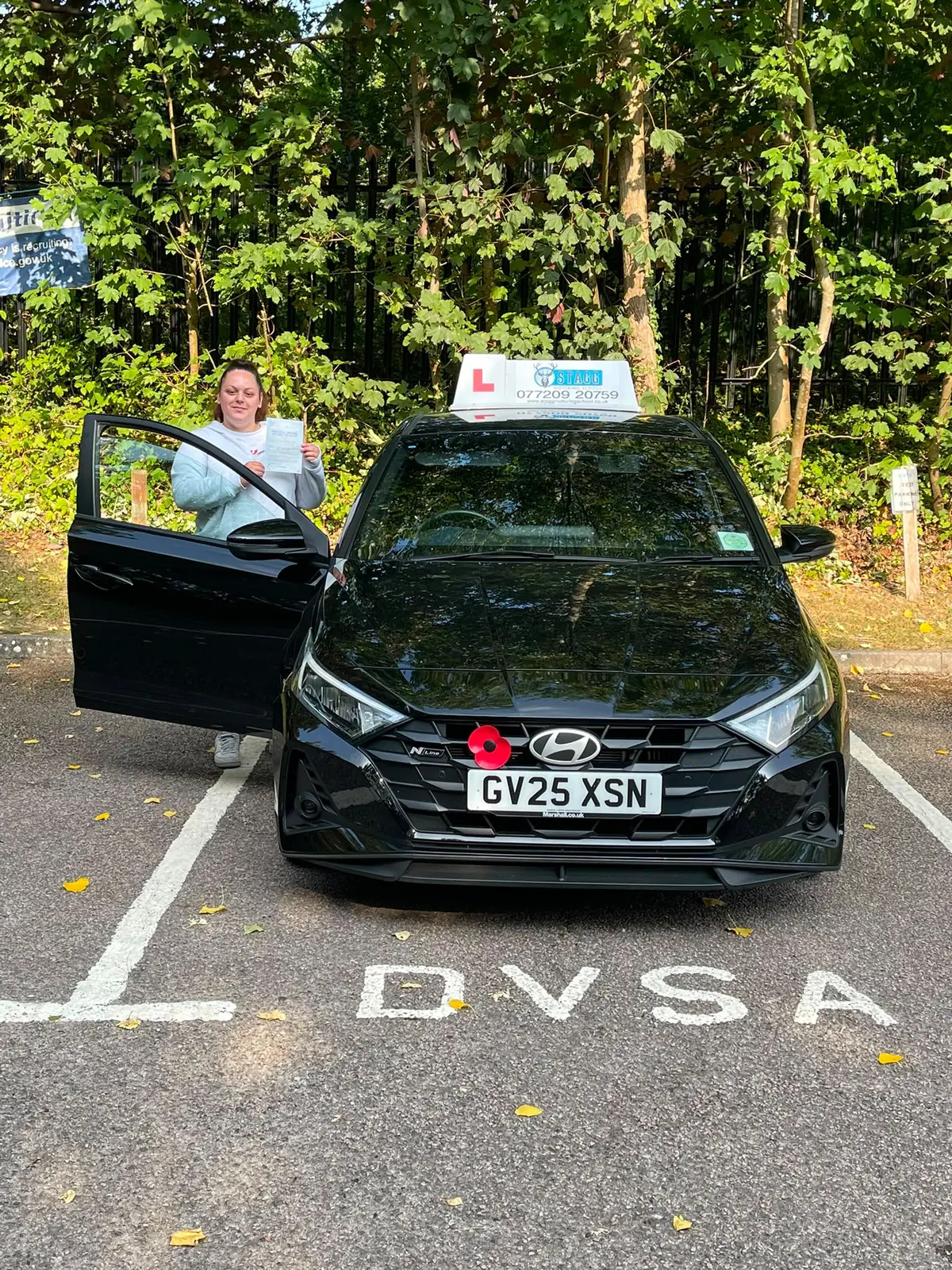 Successful Stagg Motoring School pupil holding her pass certificate beside the learner car