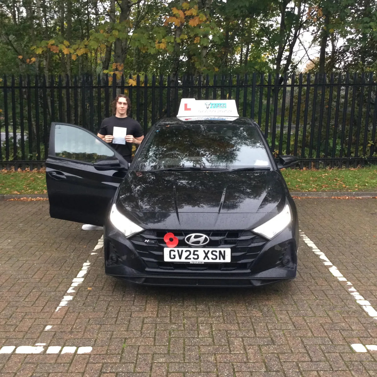 Successful driving test candidate in Crawley holding his pass certificate beside a Stagg Motoring School learner car